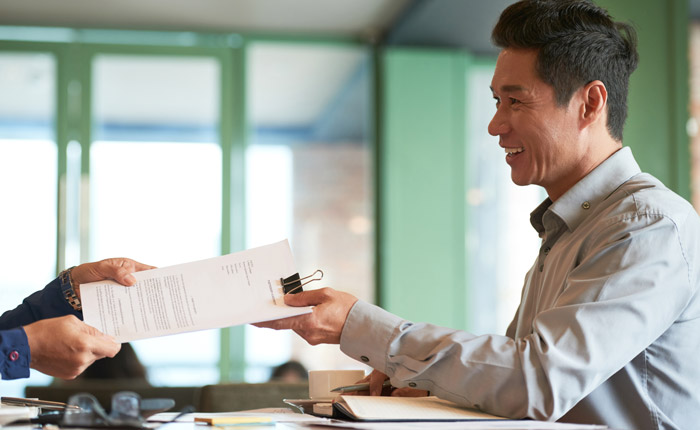 adult man smiling while handing the paper
