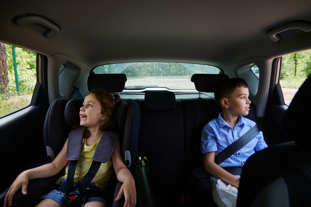 Two children, a boy and a girl, buckled in their seats while traveling in a car